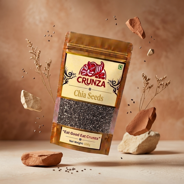A stand-up pouch of CRUNZA Chia Seeds floating against a warm beige textured background with scattered chia seeds and decorative stones around it. The package has a metallic gold-brown top and bottom, a cream label with red CRUNZA branding, and a clear window showing dark chia seeds inside.