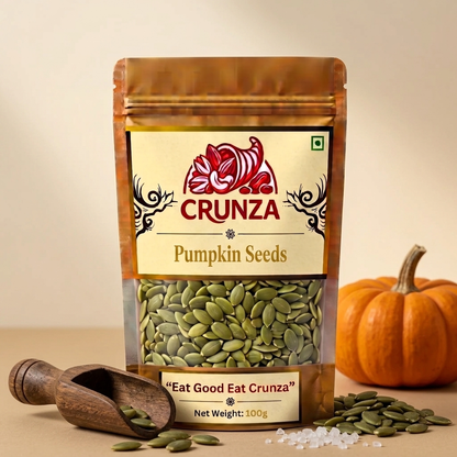 A 100g stand-up pouch of CRUNZA Pumpkin Seeds, displayed with a wooden scoop, loose seeds, and a small decorative pumpkin on a beige background.
